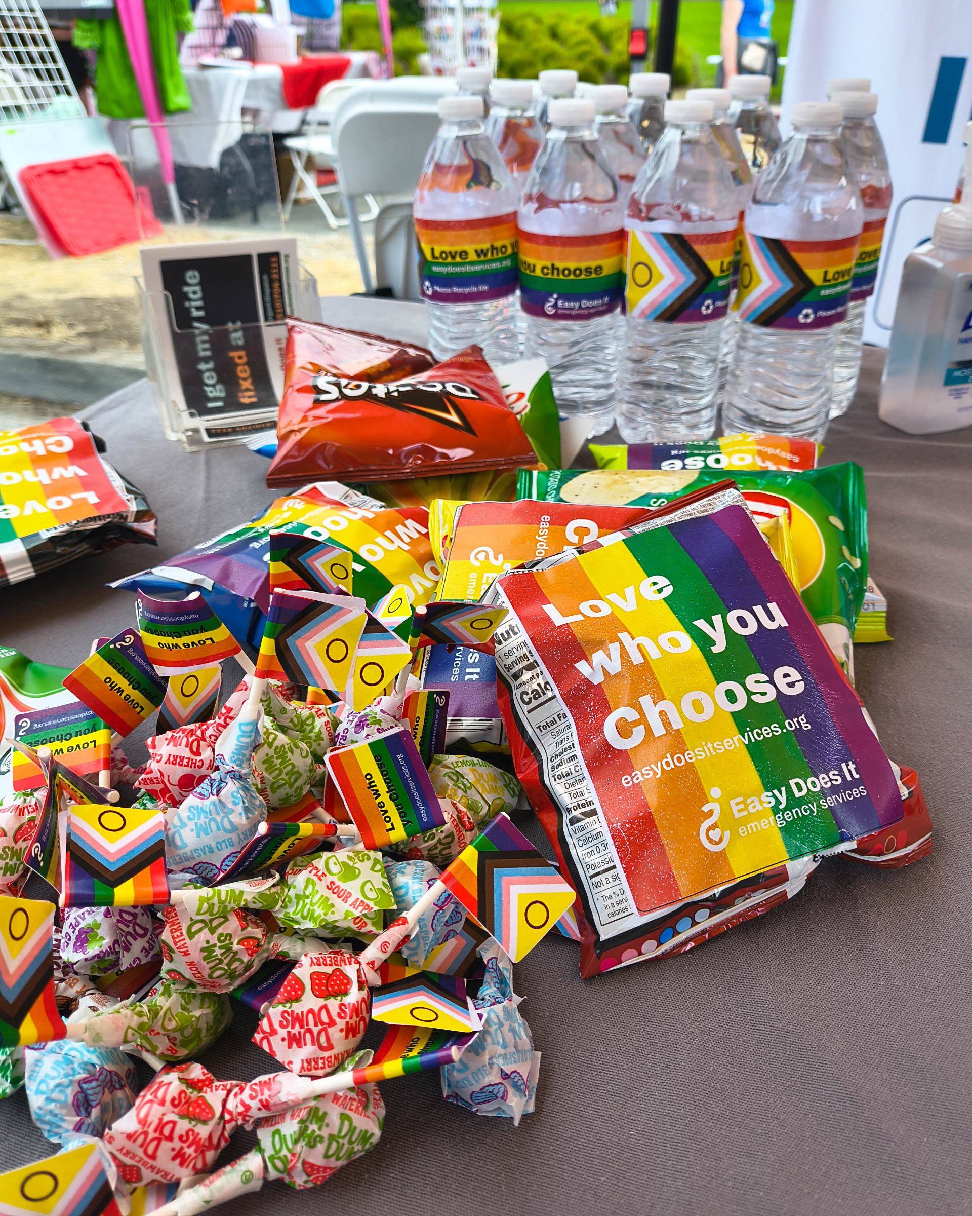 A closeup of our themed merch for Pacific Center's Pride Celebration. Water bottles, snacks, and treats with the Pride flag adhered to them, with the phrase "Love who you choose" placed atop the flag.
